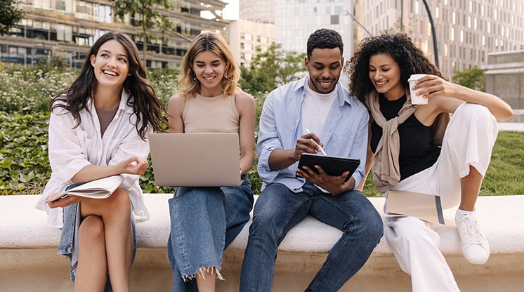 Four friends outside with laptop, ipad, and coffee